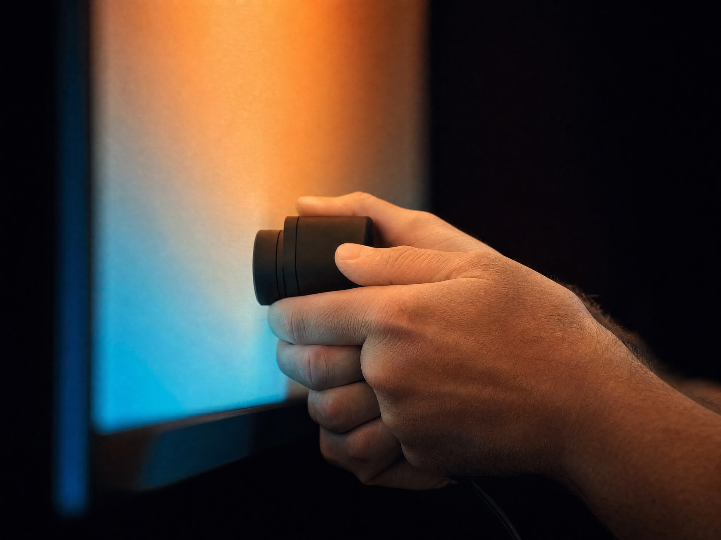 A calibrator's hands steadying a light meter against the surface of a glowing display in a darkened room
